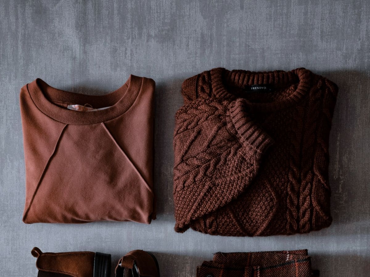 Folded knit jumpers laid flat on a grey surface, seen from above
