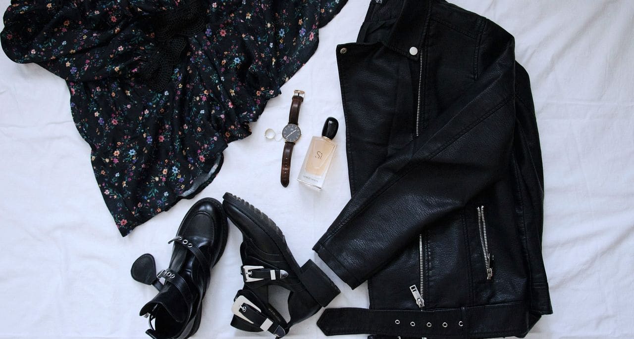 A fashion flat lay on white: a floral dress, black leather jacket, ankle boots, a watch and perfume