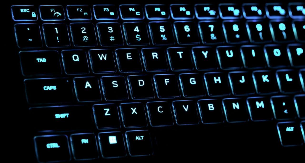 Close-up of a backlit keyboard glowing blue in a dark room
