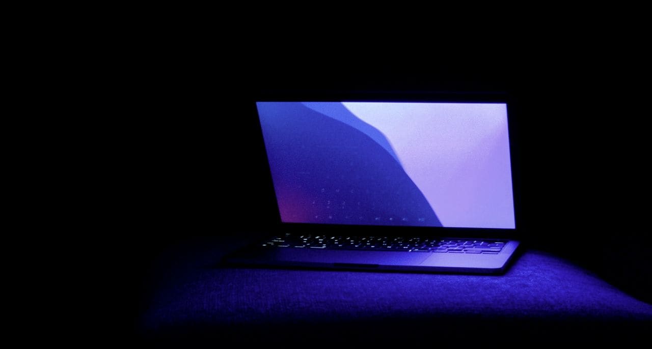 A laptop with a glowing keyboard in a dark room lit blue