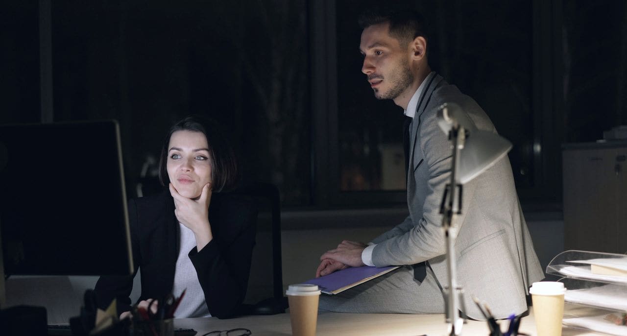 Two colleagues talking at a desk in an office in the evening