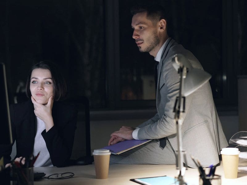 Two colleagues talking at a desk in an office in the evening